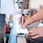 closeup of a worker using manufacturing equipment on a piece of extruded aluminum for making doors and windows